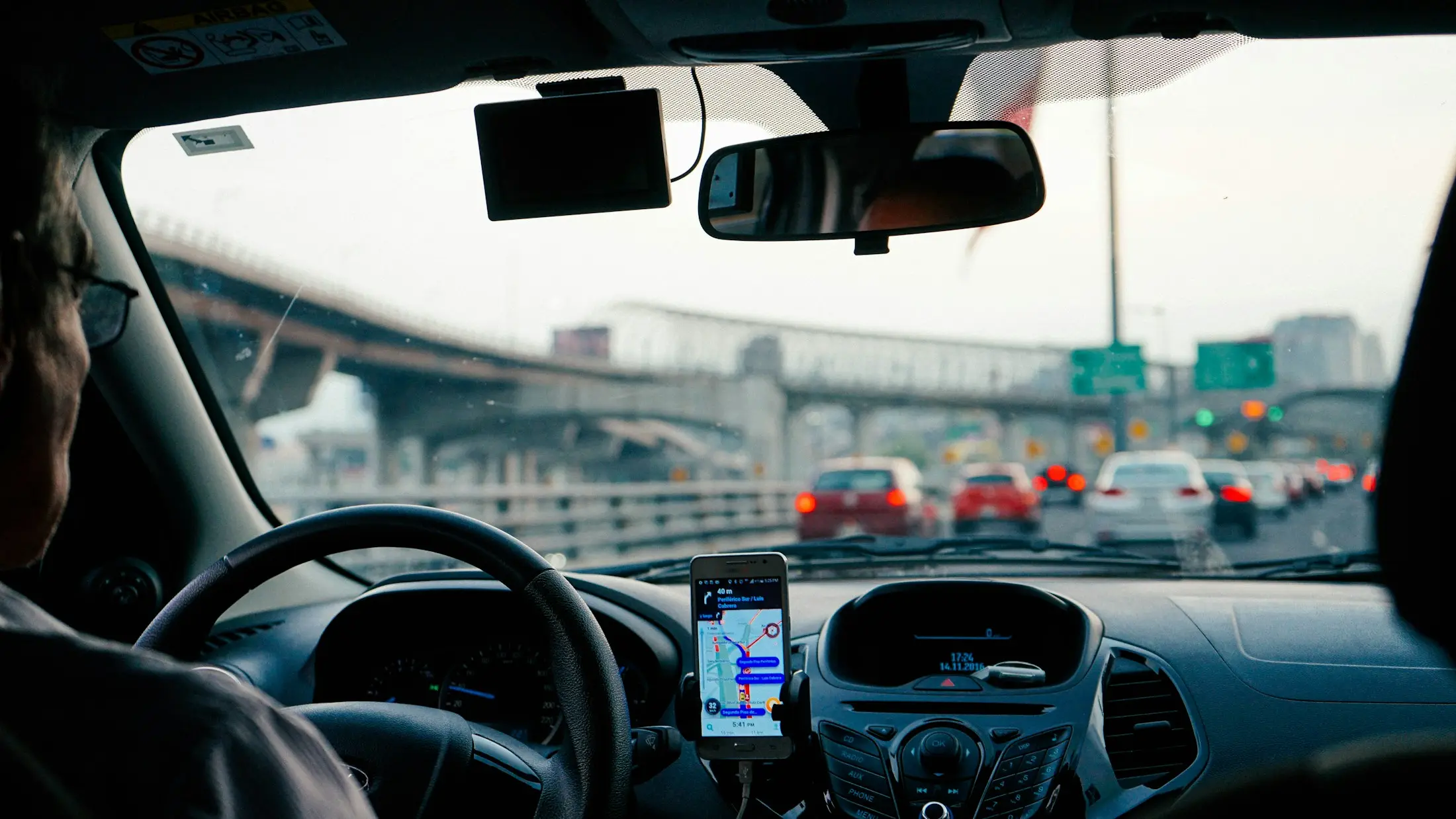 A driver on a highway flyover with a navigation app open on a phone mounted to the dashboard